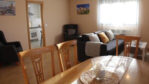 Ein Wohnzimmer mit Sofa, Sesseln, einem Esstisch und einer Küche im Hintergrund.