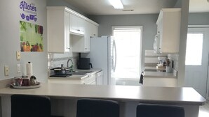 Ett modernt kök med vita skåp, en köksö med barstolar, ett stort fönster och en taklampa.