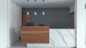 A reception desk with a wooden finish and marble base, three pendant lights, and a grey wall. - HOTEL CAMELINAS EXPRESS (Lazaro Cardenas)
