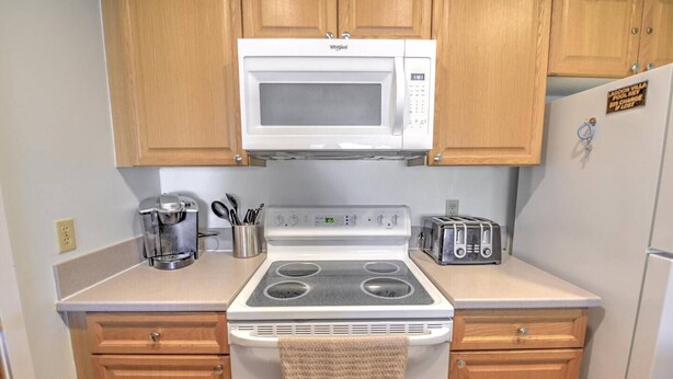 Una cocina compacta con armarios de madera, un microondas blanco, una estufa, una cafetera y un tostador.