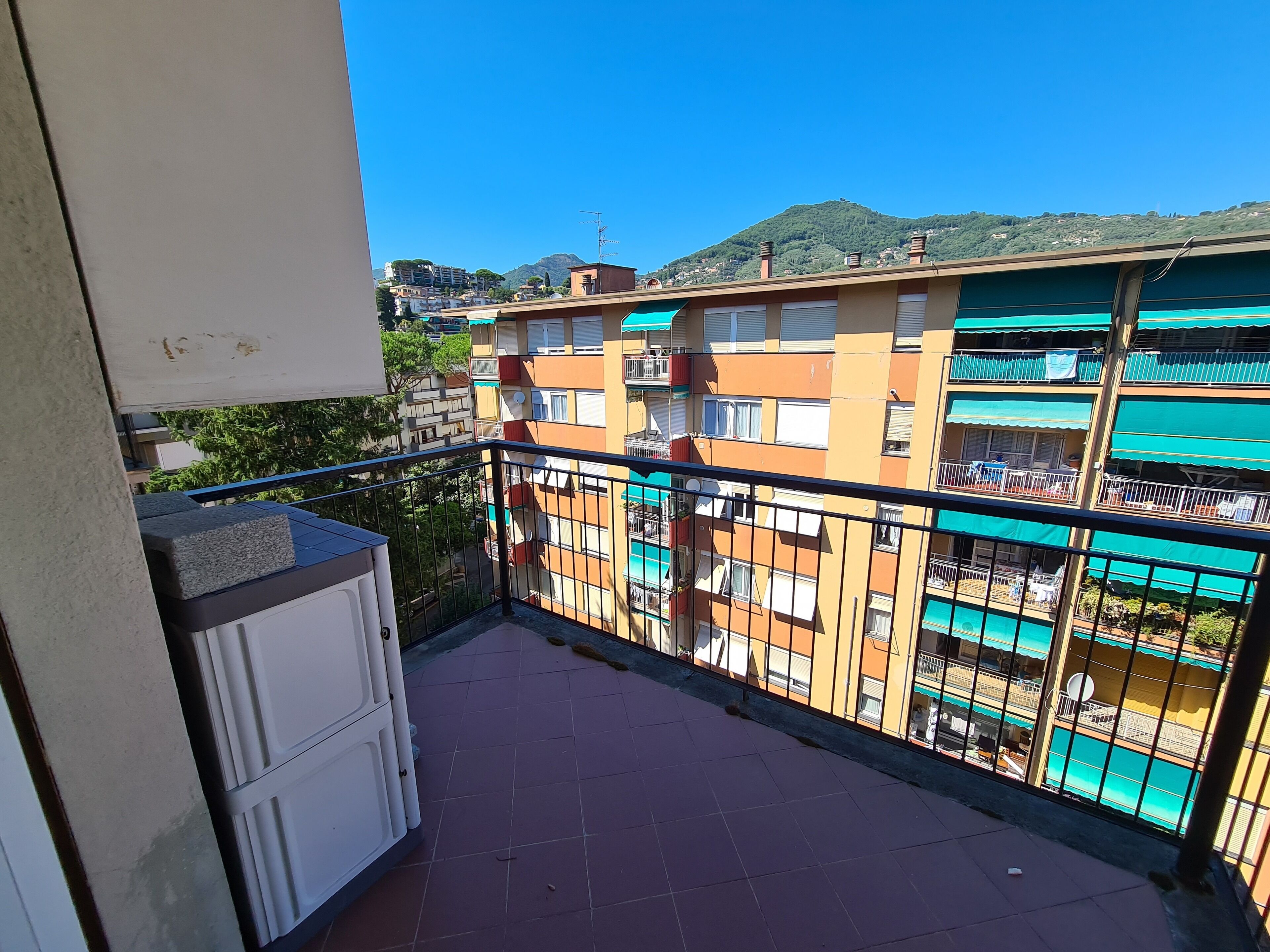A balcony with a tiled floor, a white cabinet, and a metal railing.