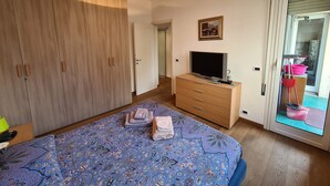 Une chambre à coucher comprenant un lit, une télévision, une armoire, une commode et une porte-fenêtre coulissante donnant sur un balcon.