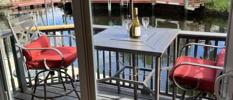 A deck with two red chairs, a table, and a bottle of champagne.