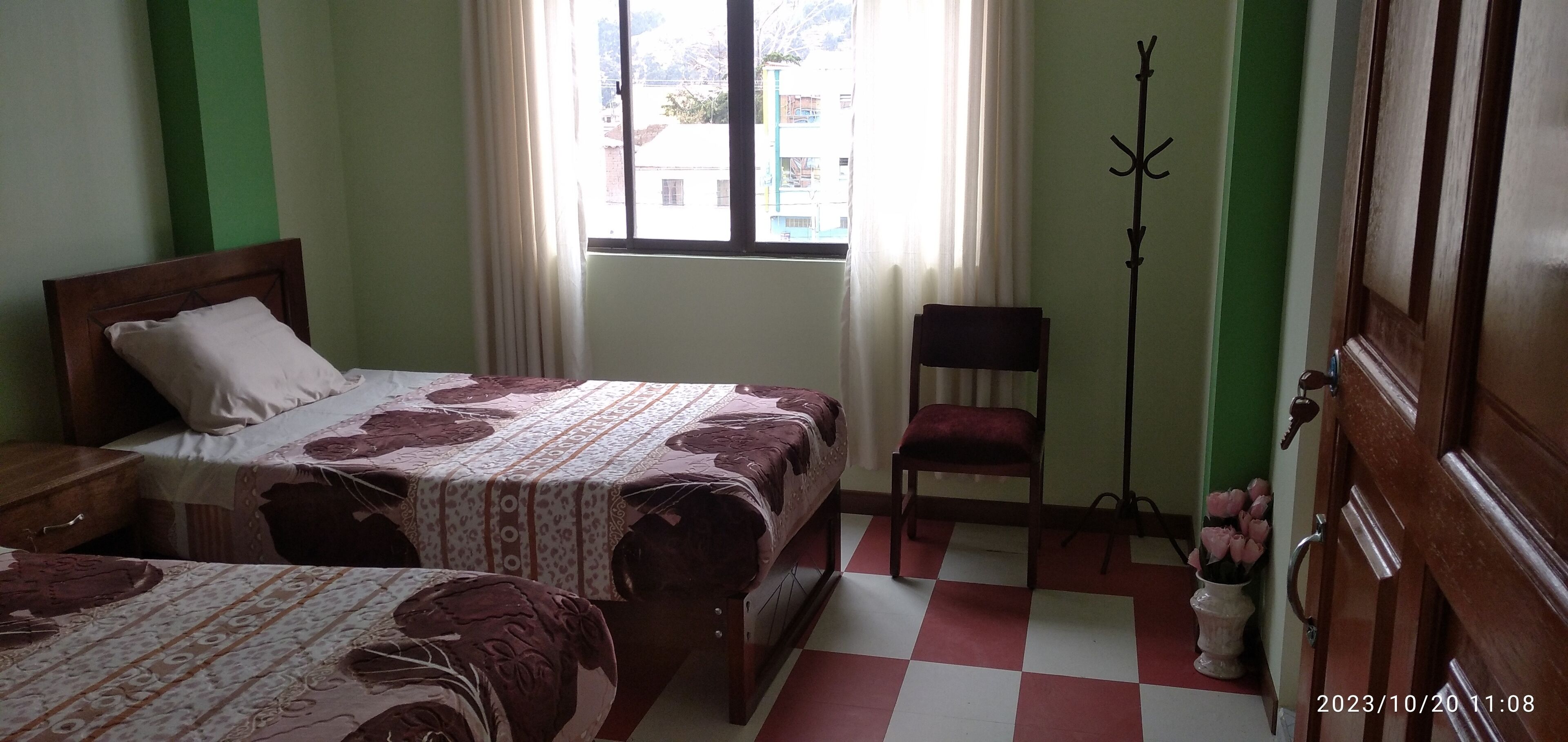 A room with two beds, a chair, a coat rack, and a window with curtains.