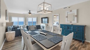 A spacious living area with a dining table, chairs, and a view of the ocean. - Emerald Isle 507 The Jolly Roger🌊Beachfront Condo w/ Views + Chair Service (Pensacola Beach)