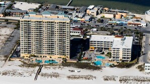 A coastal hotel with multiple buildings, including a large hotel with numerous balconies and a smaller building with a swimming pool. - Emerald Isle 507 The Jolly Roger🌊Beachfront Condo w/ Views + Chair Service (Pensacola Beach)