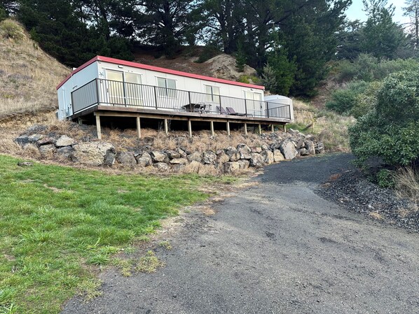 A cabin with a red roof, a balcony, and a stone foundation. - Lushingtons Bay - Takamatua (Akaroa)