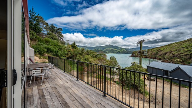 Eine Holzterrasse mit Gartenmöbeln, einem Metallgeländer und Blick auf einen See und Berge.