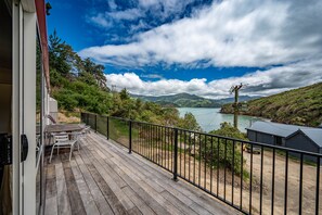 A wooden deck with outdoor furniture, a metal railing, and a view of a lake and mountains. - Lushingtons Bay - Takamatua (Akaroa)