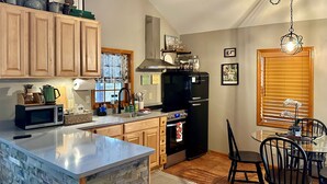 Una cocina con armarios de madera, una isla integrada, un refrigerador negro y un comedor con sillas negras.