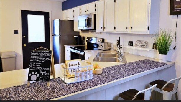 A modern kitchen with white cabinets, a microwave, a refrigerator, and a sink. There's a chalkboard with writing and a tray with a sign that says "Penn State".