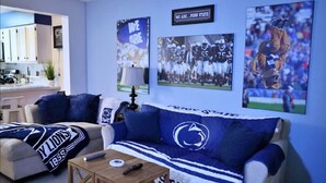 A living room with a couch covered in a Penn State Lions blanket, a coffee table, and a TV displaying sports images.