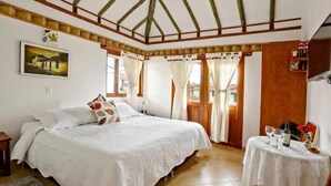 Un dormitorio con una cama grande, una mesita con vasos y una botella, y un cuadro en la pared.
