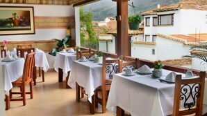 Un restaurante con terraza, manteles blancos, sillas de madera y vistas de los edificios y colinas circundantes.