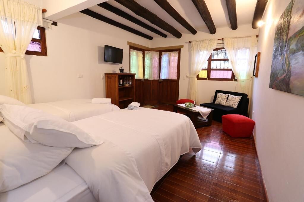 Une chambre avec deux lits, une armoire en bois, un téléviseur et un fauteuil rouge.