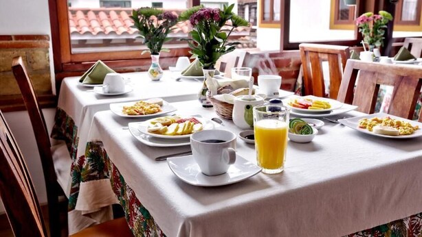 Una mesa de desayuno preparada con platos de comida, tazas y un vaso de jugo de naranja.