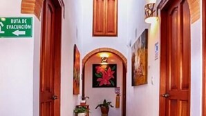 Un pasillo con una puerta de madera a la izquierda, un letrero verde que indica una ruta de evacuación y un suelo de baldosas con un borde estampado.