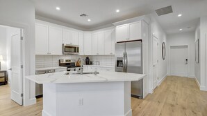 A modern kitchen with white cabinetry, a central island, stainless steel appliances, and a wooden floor.