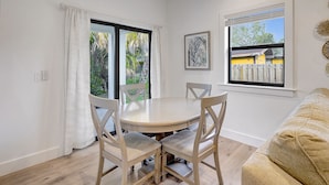 A dining area with a round table and four chairs, a window with a view of a wooden fence, and a framed picture on the wall.