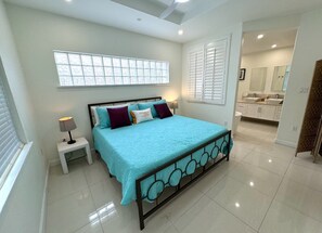 A bedroom with a bed, nightstands, a window, and a bathroom visible in the background.