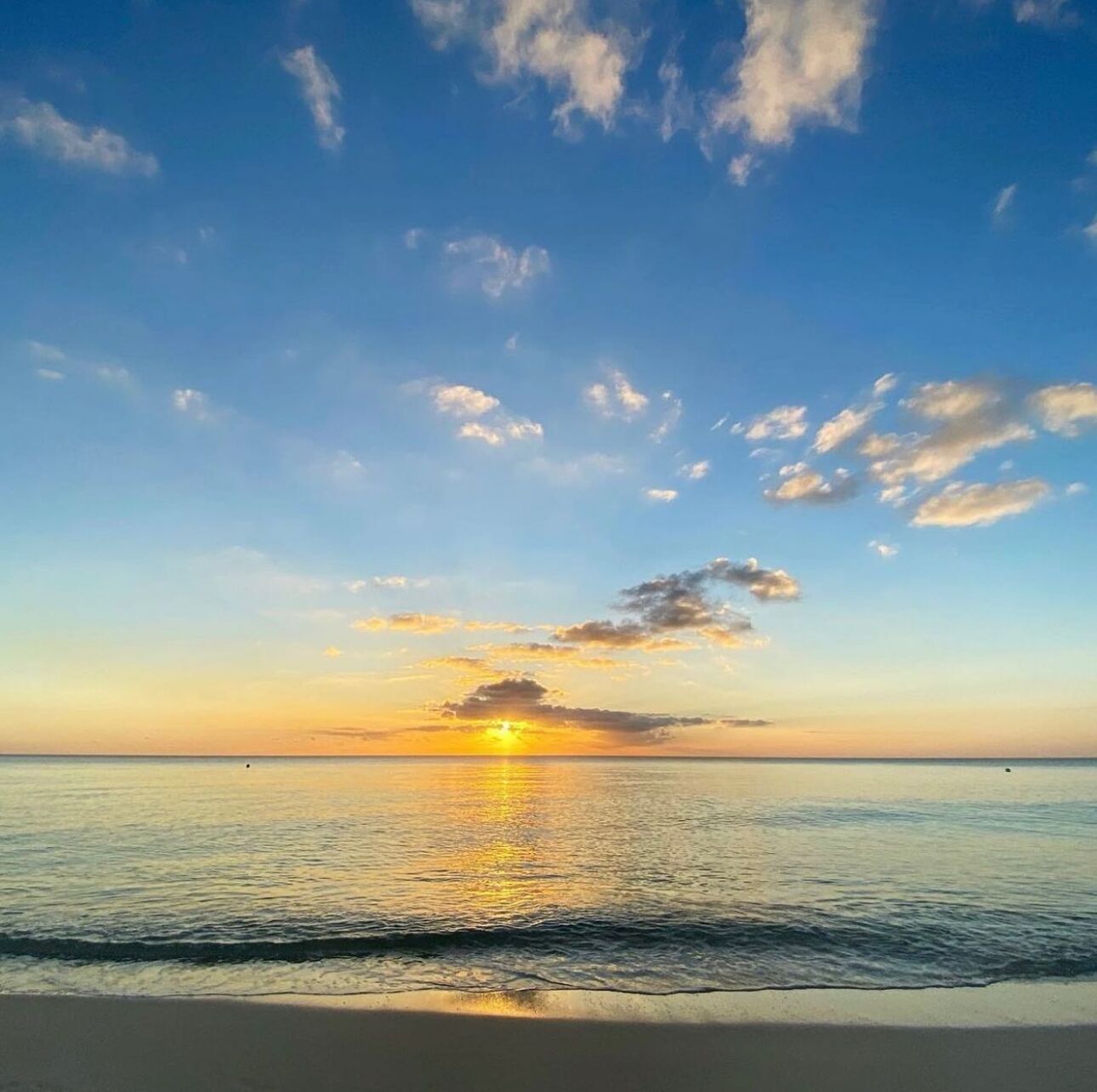 A beach scene with a sunset over the ocean, clear sky, and calm water.