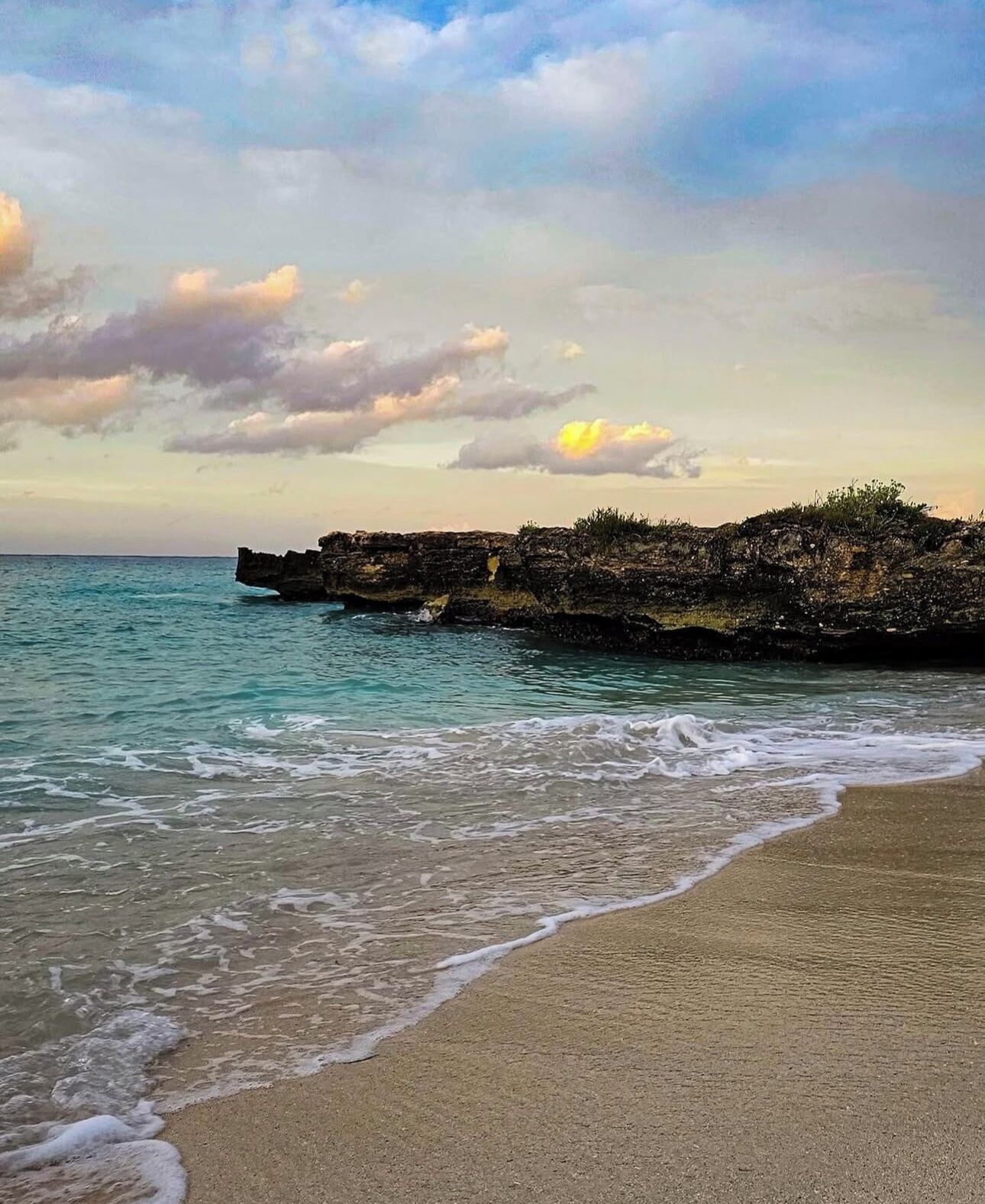 A beach with a rocky outcrop and calm sea.