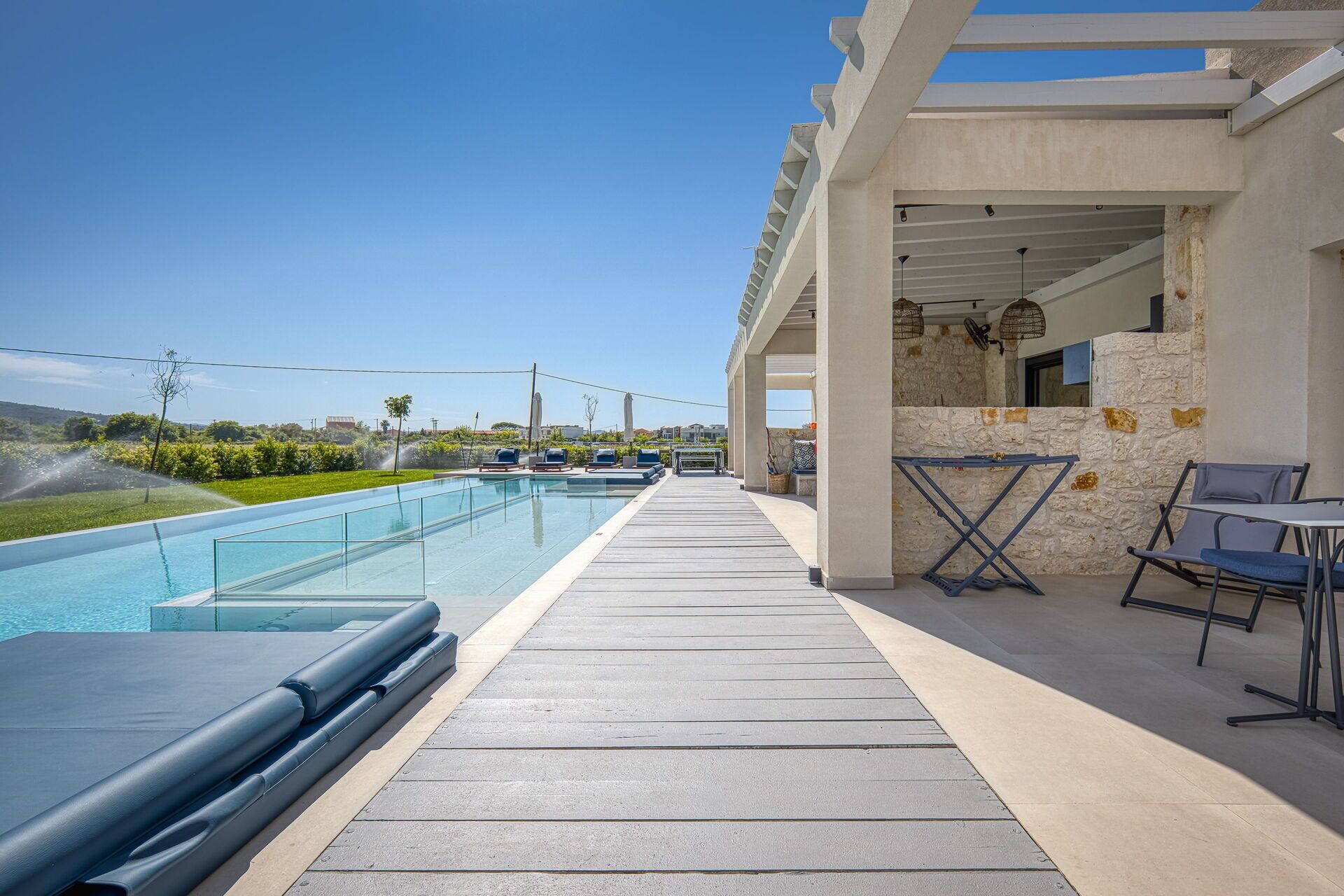 Un área de piscina moderna al aire libre con vistas despejadas del paisaje, una zona de estar cubierta con sillas y un muro de piedra.