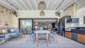 Un espace de restauration moderne avec une table centrale, des chaises bleues et des ventilateurs de plafond en osier.