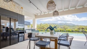 Une cuisine extérieure moderne avec un espace repas offrant une vue sur une piscine et des montagnes.