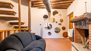 Un interior acogedor con un sillón negro, vigas de madera, una chimenea de ladrillo y espejos redondos en la pared.