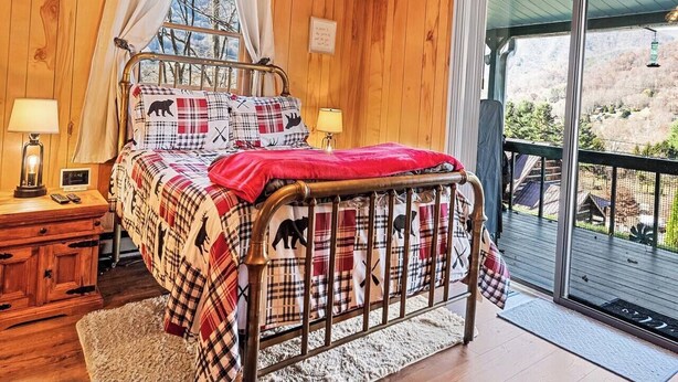 A wooden-paneled bedroom with a bed, bedside tables, and a view of the outdoors. - Lazy Bear Lodge-Breathtaking Views! Pet Friendly (Maggie Valley)