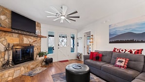 A living room with a stone fireplace, a ceiling fan, and a couch with decorative pillows. - Lazy Bear Lodge-Breathtaking Views! Pet Friendly (Maggie Valley)