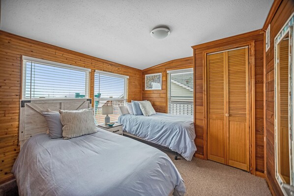 A bedroom with two beds, wooden walls, a ceiling light, and a window.