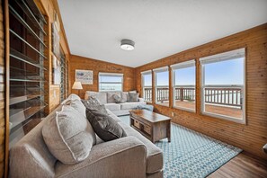 A cozy living room with a large window overlooking a balcony, a wooden interior, and a comfortable sofa.