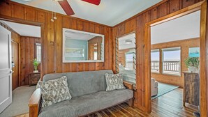 Ein gemütliches Zimmer mit Holzwänden, einem grauen Sofa mit gemusterten Kissen und einem großen Spiegel.