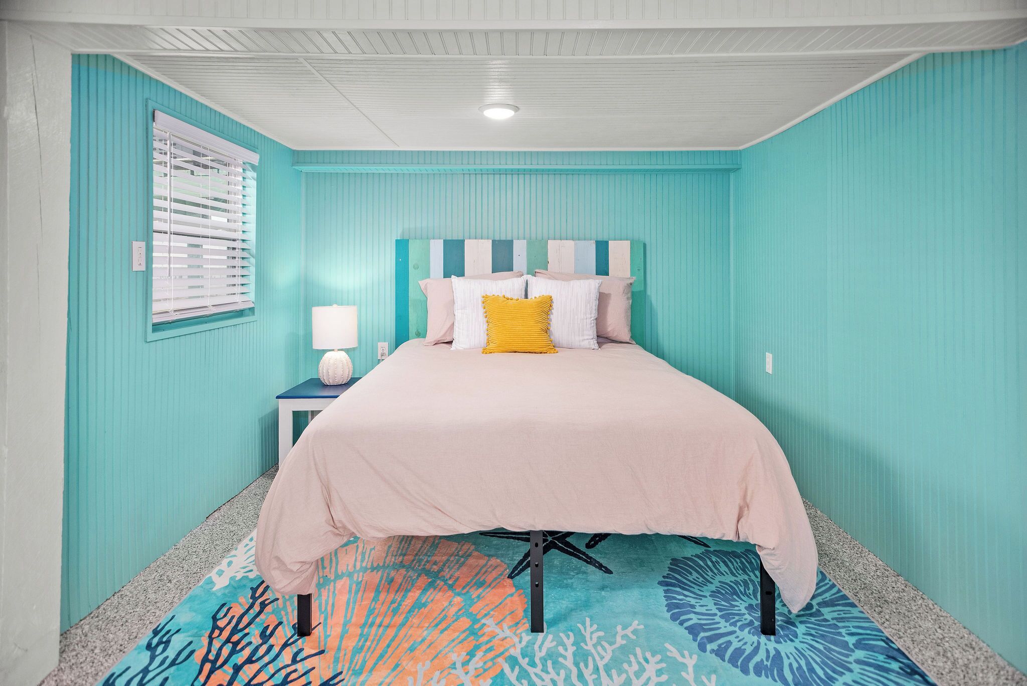 A bedroom with teal walls, a bed with a striped headboard, and a coral-patterned rug.
