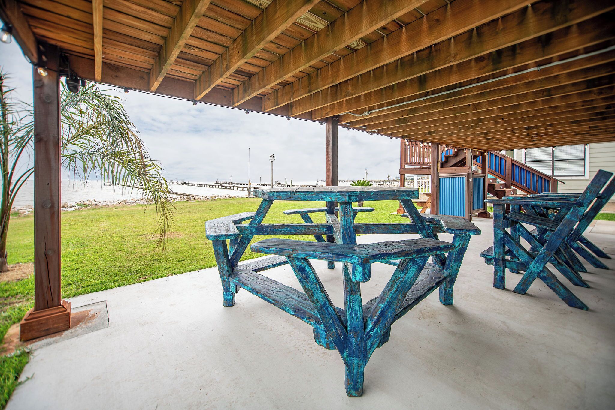An outdoor covered patio with a picnic table and chairs, a view of the ocean, and a wooden deck.