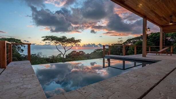 A pool with a clear view of the sunset over the ocean, surrounded by wooden structures and stone flooring. - Vista Sirena: Expansive Ocean View 4 bedroom / 4.5 bath home above Dominical (Puntarenas Province)