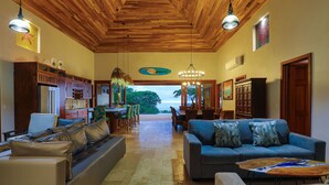 A spacious living area with a wooden ceiling, a blue sofa, and a dining area with chairs and a table. - Vista Sirena: Expansive Ocean View 4 bedroom / 4.5 bath home above Dominical (Puntarenas Province)