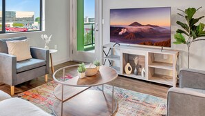 A modern living room with a large flat-screen TV, a grey sofa, a round coffee table, and a colorful rug. - BRAND NEW! 2BR Apt near Disney and SNA! Pool & Gym
 (Santa Ana)
