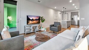 A modern living room with a sofa, armchair, and coffee table. There is a flat-screen TV on a stand, a plant, and artwork on the walls. - BRAND NEW! 2BR Apt near Disney and SNA! Pool & Gym
 (Santa Ana)
