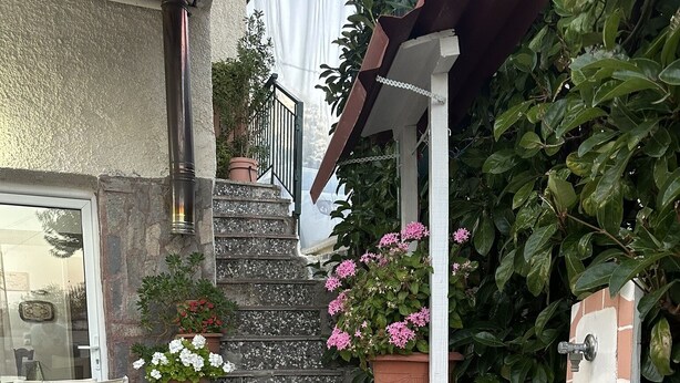 Eine terrasse mit Steinpflasterung, Terrakotta-Pflanzgefäßen, einem Holztisch und einem Stuhl.