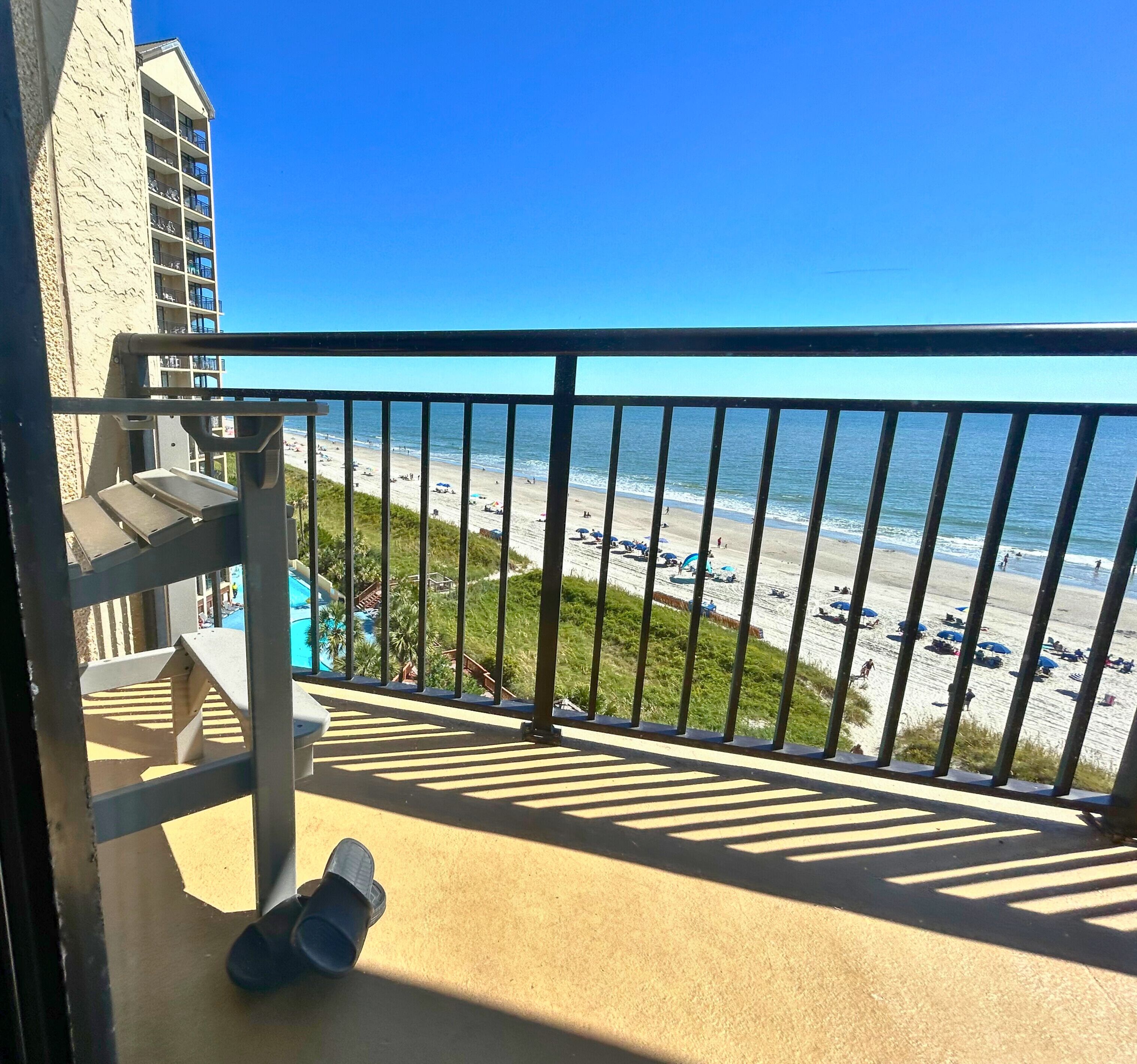 A balcony with a view of a beach and a pool area.