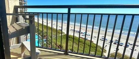 A balcony with a view of a beach and a pool area.