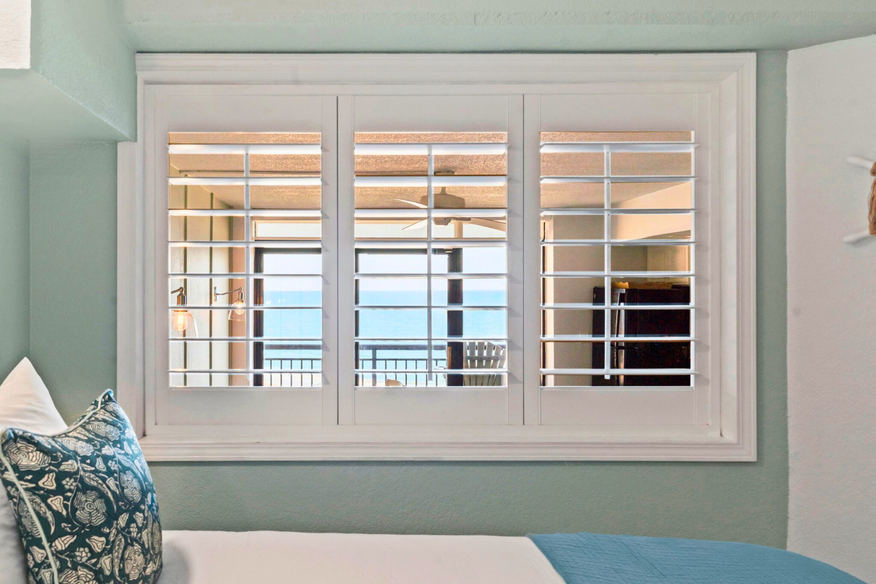 A bedroom with a large window, a bed, and a view of the balcony.
