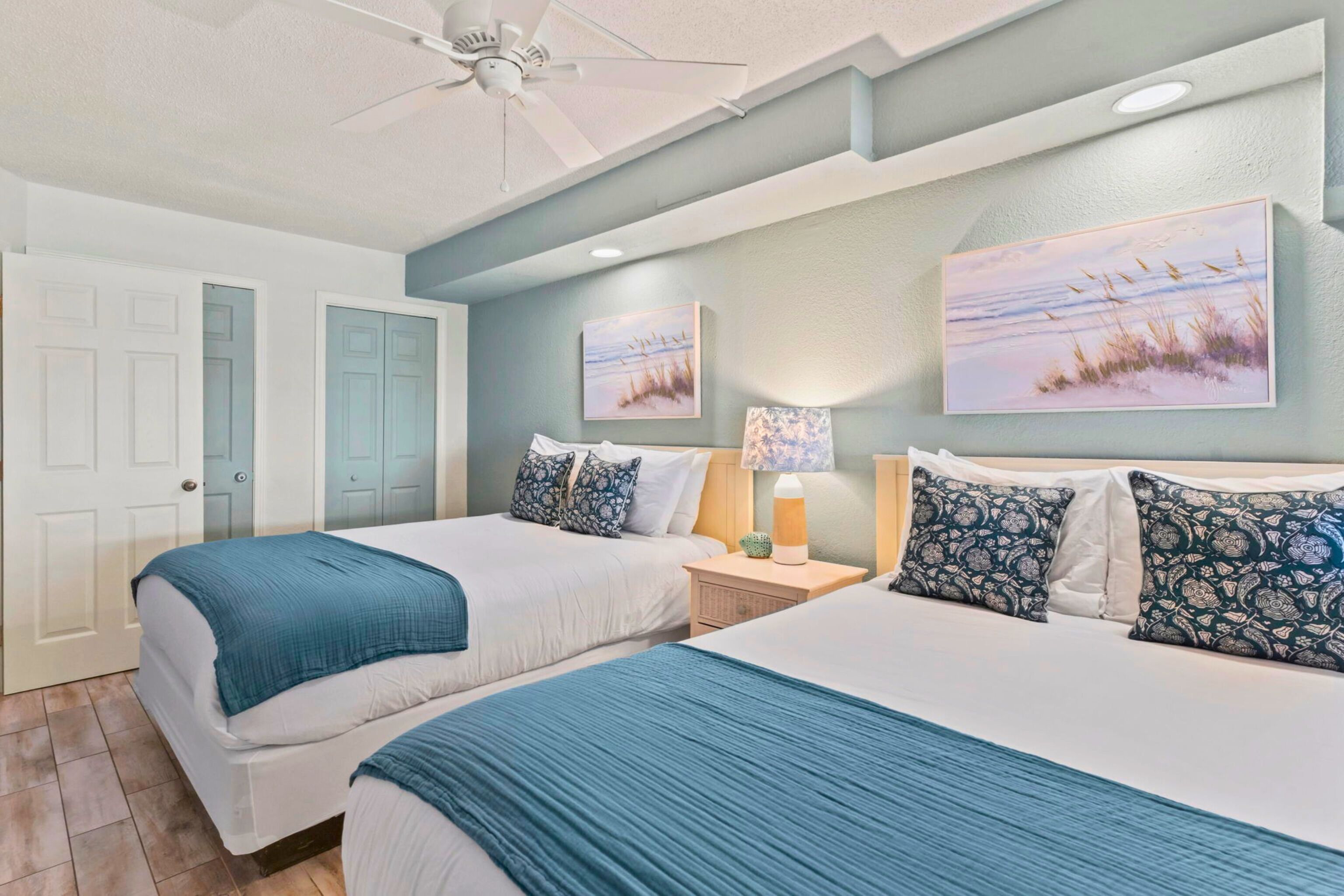 A bedroom with two beds, a ceiling fan, and artwork on the walls.