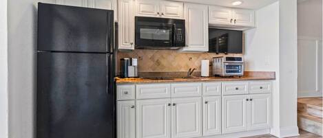 Una cocina con armarios blancos, un refrigerador negro, un microondas y un horno empotrado.