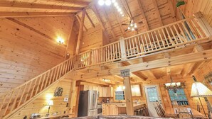 Een ruime hut met een hoge plafond, houten inrichting, een balkon, een keukenhoek en een eethoek.