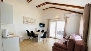 Una sala de estar moderna con un sofá, una mesa de comedor con sillas, un televisor de pantalla plana y un amplio ventanal con cortinas.