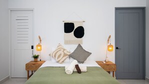 Une chambre à coucher bien rangée, avec un lit, des oreillers, une tapisserie murale, des lampes de chevet et une porte.